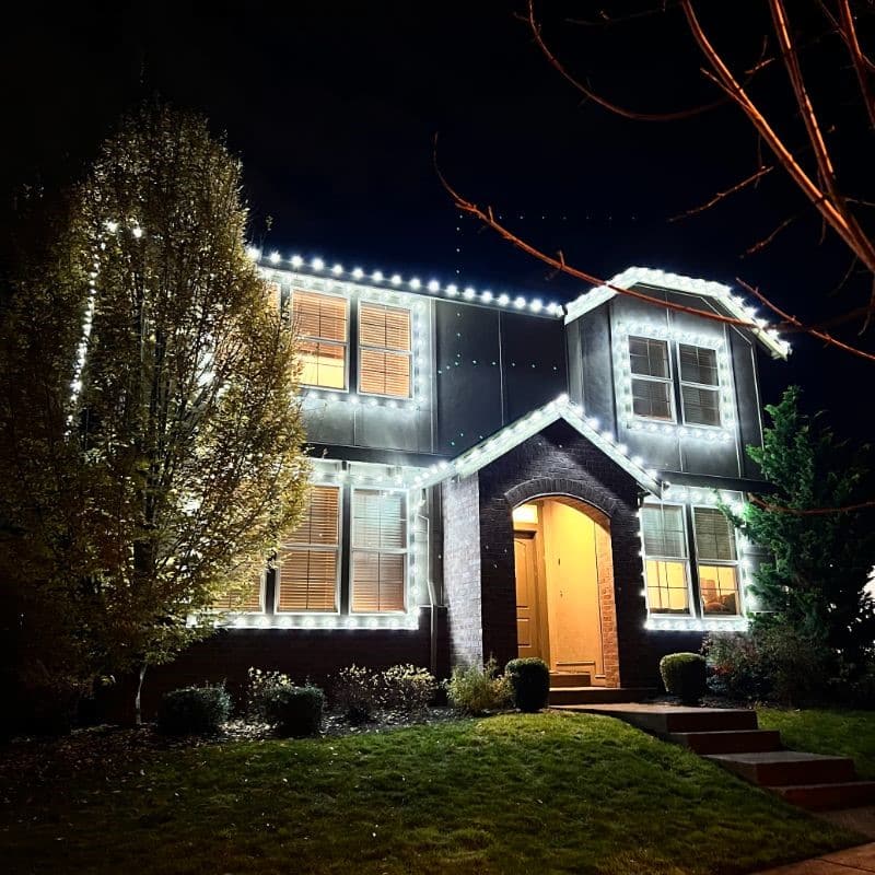 House decked out in bright white Christmas lighting. This Portland, OR home is ready for the holidays with lights outlining the roofline, windows, and tree.