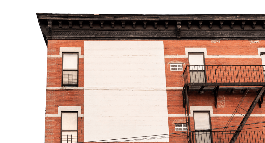 Red brick building with a large white painted-over area where graffiti was removed. Black fire escape and decorative cornice. Graffiti Removal in Portland OR.
