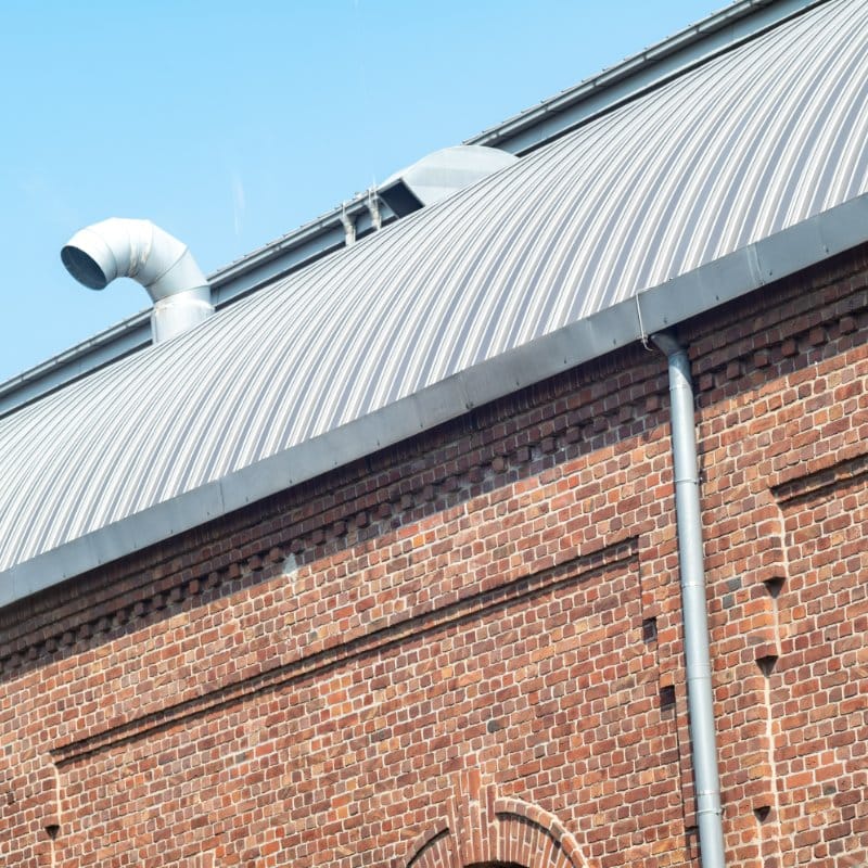 Red brick building with a curved metal roof and a downspout, showcasing a structure that may require commercial gutter cleaning.