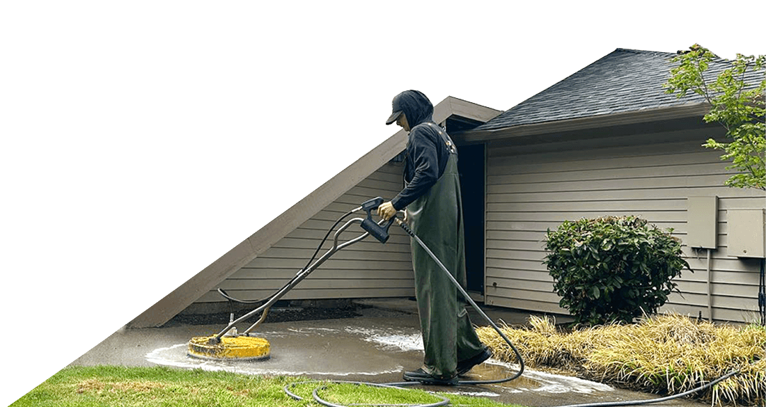 A professional is pressure washing a concrete surface in Portland, OR. He is wearing protective gear and using a surface cleaner attachment for efficient cleaning. Pressure washing removes dirt and grime effectively.