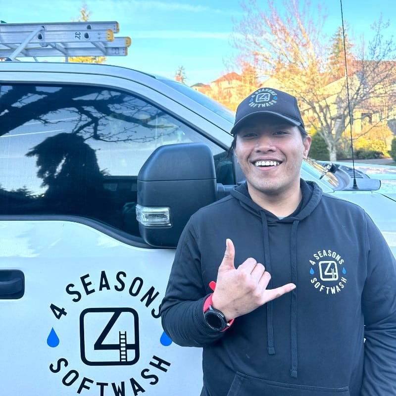 Meet Our Team: Smiling technician from 4 Seasons Softwash gives a "hang loose" hand gesture in front of company truck with logo. Ladders visible on the truck rack.