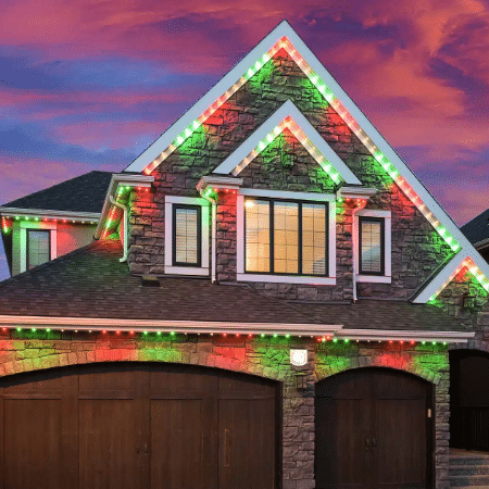 Luxury home in Portland, OR, adorned with permanent holiday lighting in red and green, installed along the roofline and gables, set against a vivid sunset sky.
