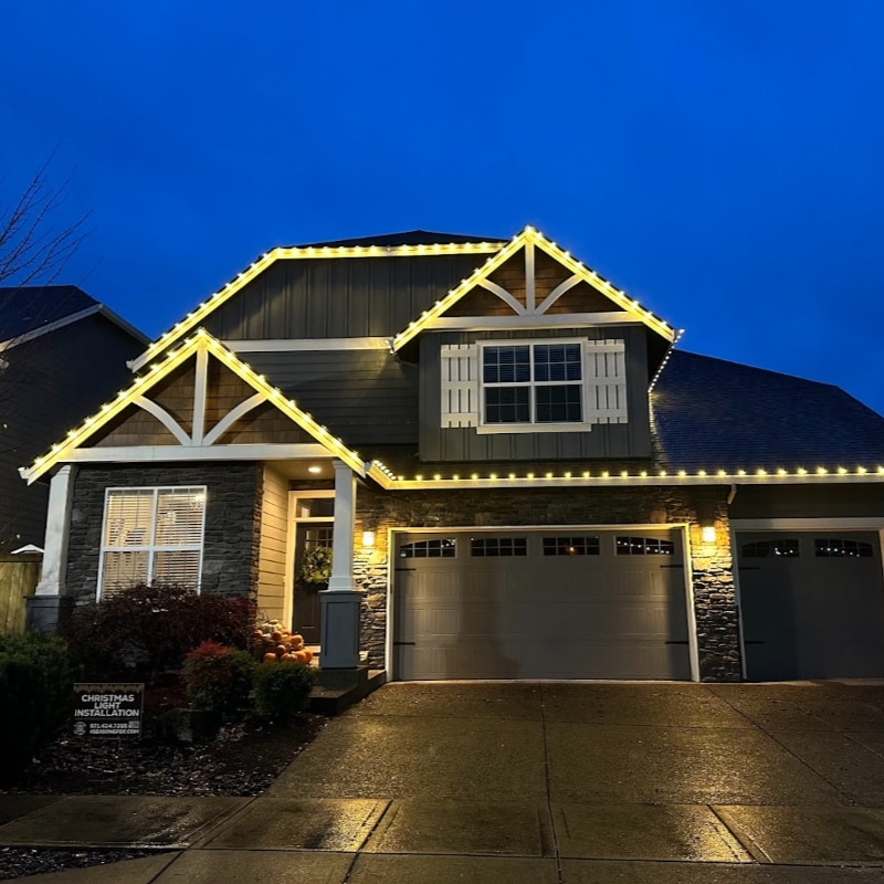 Beautiful home adorned with Christmas lighting, highlighting the roofline and gables. Warm, inviting glow against a twilight sky. Christmas Lighting installation advertisement in the yard.