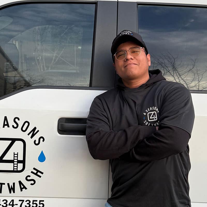 Meet our team: A smiling man wearing glasses and a "4 Seasons Softwash" hoodie stands confidently with arms crossed in front of a company vehicle. The logo is visible on the van and hoodie.