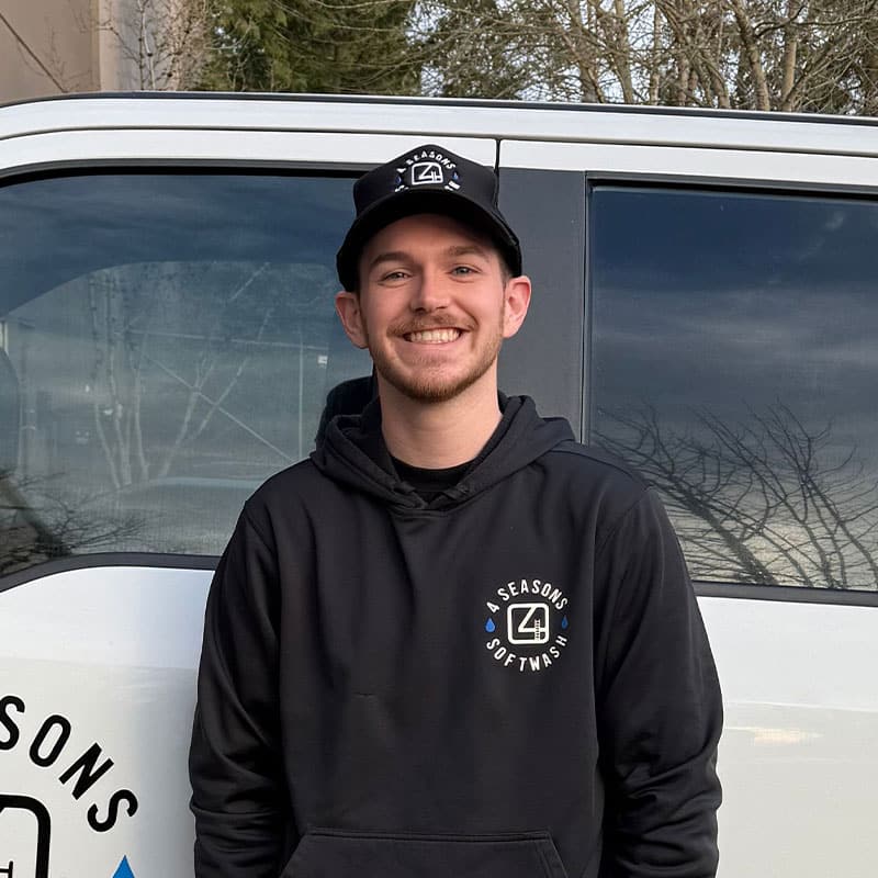 Smiling man in a "4 Seasons Softwash" hoodie and hat stands in front of a company truck. This team member is featured in our blog post.